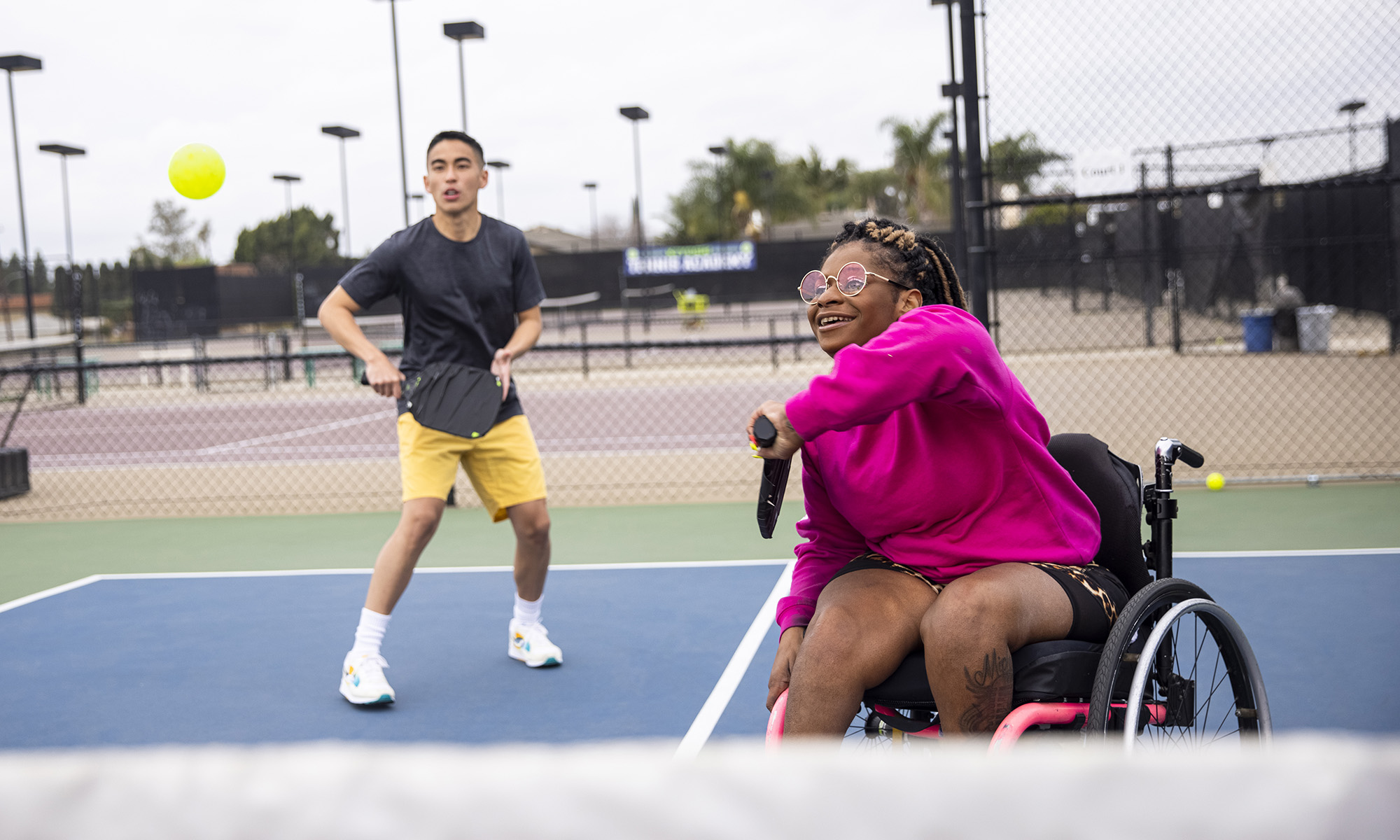 A young black disabled woman playing pickleball with her friend.